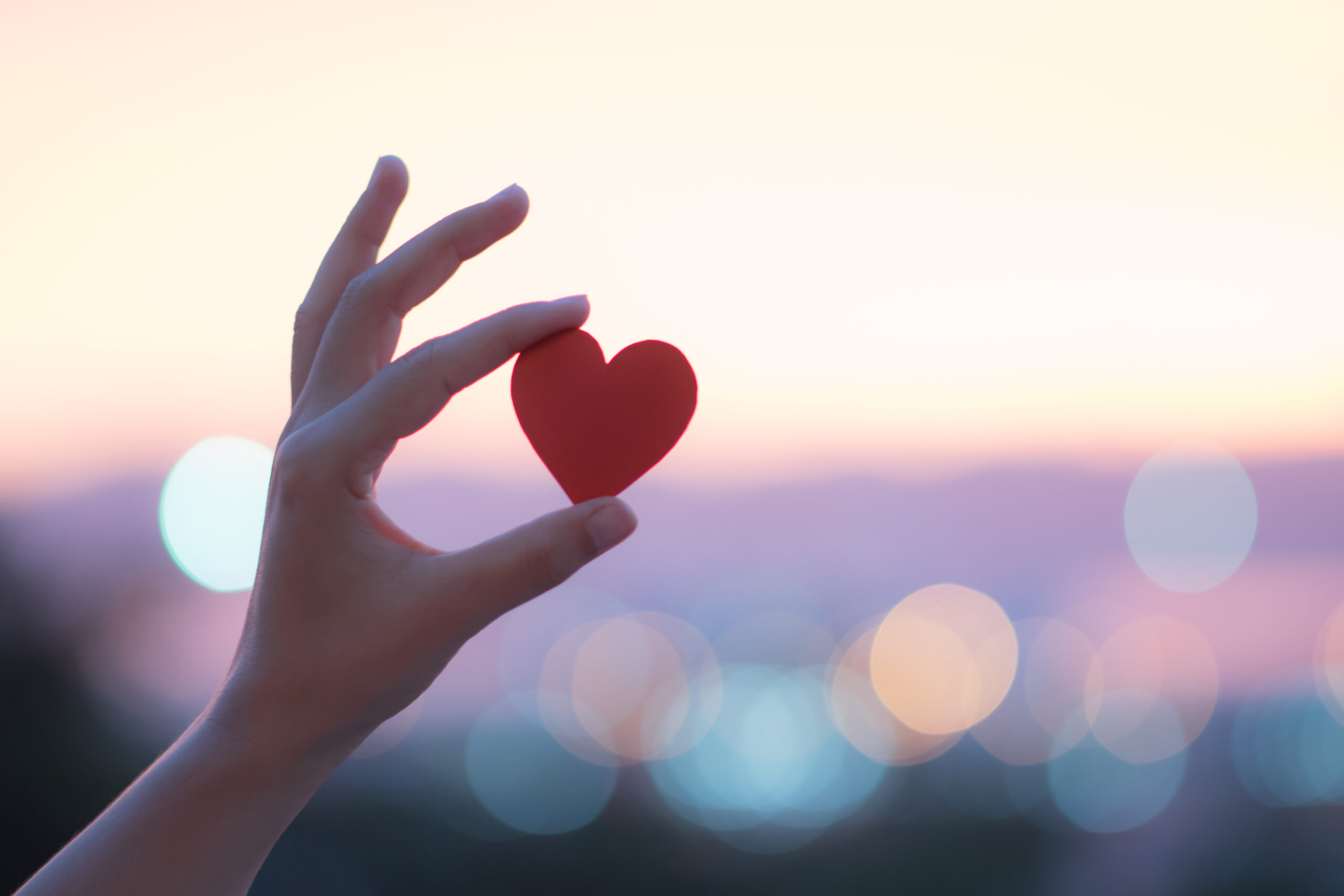 macro close up of hand holding a heart with blurry city lights in background